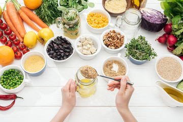 cropped view of woman adding seeds in glass jar with salad on wooden white table