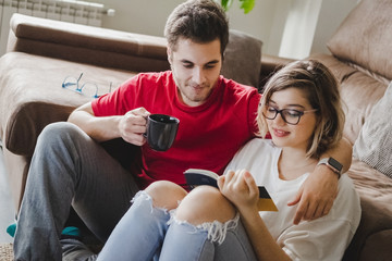 A couple reads a book and drinks coffee on the couch at home