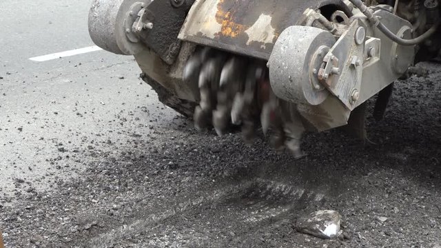Road milling machine cuts the old asphalt. Road repair. Destruction of the road surface. The cutter cuts a layer of asphalt. Pieces of stone fly apart. Close-up