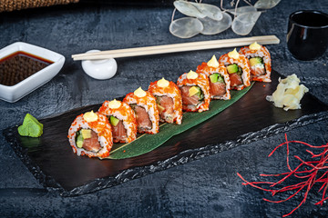 Close up view on set of sushi roll. California roll with salmon, avocado and caviar served on black stone on dark background. Japanese cuisine. Copy space. Served sushi for menu. Healthy food, seafood