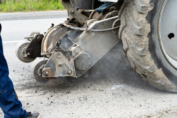 Road milling machine cuts the old asphalt. Road repair. Destruction of the road surface. The cutter cuts a layer of asphalt. Pieces of stone fly apart. Close-up