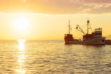 Fototapeta premium Fishing trawler at sunrise moored in the beautiful harbor of a small town Postira - Croatia, island Brac