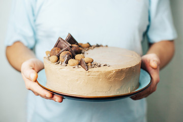 Chocolate cake in male hands on a blue plate. Sweet gift. Birthday. Valentine's Day. Chef. Homemade baking. Sponge cake with cream.