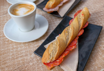 Open-air breakfast. Classic Mediterranean breakfast. Coffee with milk, sandwich with spanish ham, sandwich with chorizo. Breakfast on the outdoor terrace in the street cafe. Summer time.