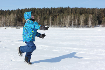 Fototapeta na wymiar Happy cheerful boy with a snowball in his hand running through the snow