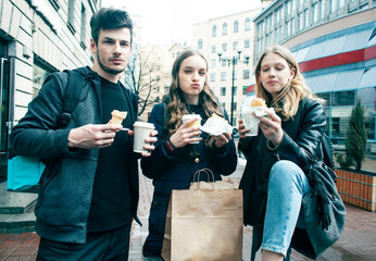 lifestyle and people concept: two girls and guy eating fast food on city street together having fun, drinking coffee