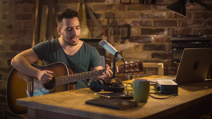 Young man is singing and playing guitar while making an audio recording at home in a garage.