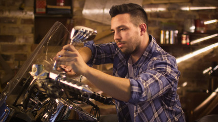 Man is tightening nuts with a spanner and repairing his motorcycle in a garage.