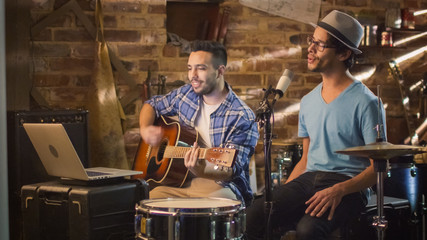 Two young man sing and play guitar while recording a song in a home studio in a garage.
