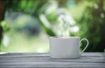 Hot coffee cup with white the wooden table and the Green leaf background with copy space on left