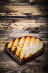 Grilled bread on burned wooden table. Preparing for traditional rural dinner. Toned