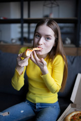 Funny brunette girl in yellow sweater eating pizza at home