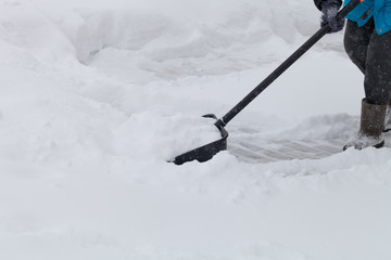 Old woman in warm blue jacket clears a snowdrifts with a snow shovel