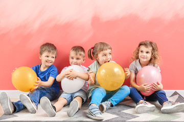 Fototapeta na wymiar Cute little children with air balloons sitting near color wall