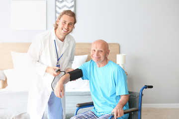 Obraz premium Doctor measuring pressure of elderly man in nursing home