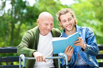 Young man reading book to his elderly father in park - Powered by Adobe