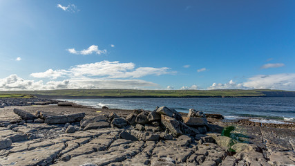 Spectacular bare limestone landscape and ocean in Doolin Bay with the Cliffs of Moher in the background, next to the pier, Wild Atlantic Way, beautiful sunny spring day in County Clare in Ireland
