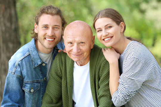 Relatives With Elderly Man Walking In Park