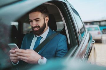 Young smiling handsome Caucasian businessman in blue suit sitting in his expensive with seat belt...