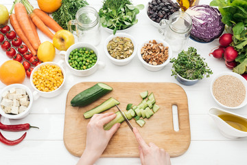 cropped view of woman chopping cucumber on wooden white table