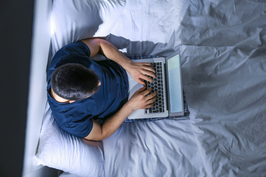 Young Man With Laptop In Bed At Night, Top View