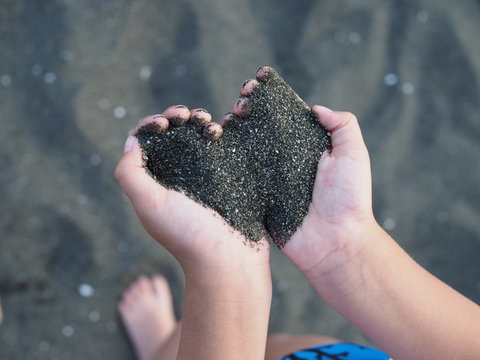 black sand in children's hands in the form of a heart