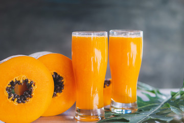 papaya slice and papaya juice on green leaf and wooden background, healthy and diet fruit 