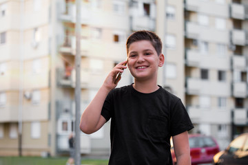 Teenage boy smiling while talking with his friends via social networks using mobile phone, sitting against urban landscape background