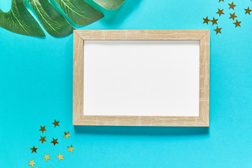 Photoframe with golden glitter confetti stars and monstera leaves on blue background. Festive flat lay. Mock up for you projects