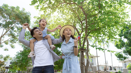 Happy Asian family. Father gave his daughter a piggyback at a park at natural sunlight background and house. Family vacation concept with copy space