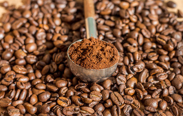 measuring spoon with ground coffee on the background of roasted arabica coffee beans