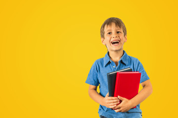 Happy pupil schoolboy with books on yellow background.