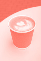 Coral color paper cup of coffee take-away on table with copy space.