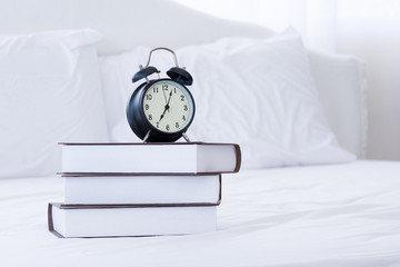 Books and alarm clocks on the white bed.