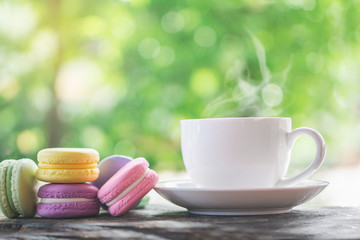 colorful macarons with hot coffee cup over nature garden in background