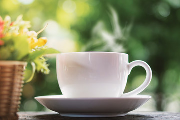 hot coffee cup on wooden table over nature green background with morning sunlight 