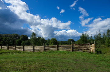 Fototapeta na wymiar Wooden fence set in a forest area in the background of a blue sky with clouds