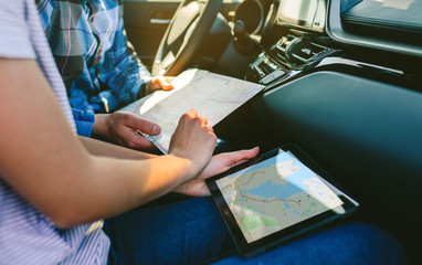 Young couple comparing a paper map and a gps navigator on the tablet sitting in the car