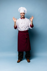 Positive professional happy man chef showing tasty ok sign isolated on light blue.