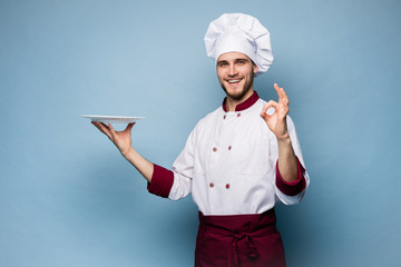 Positive professional happy man chef showing tasty ok sign isolated on light blue.
