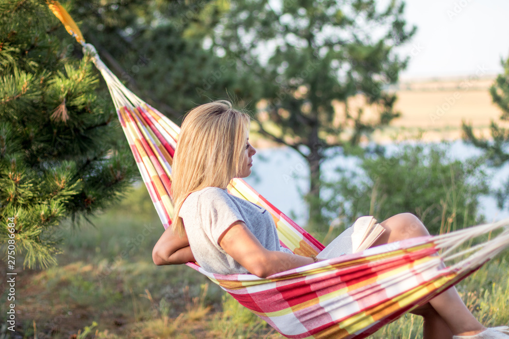 Canvas Prints young attractive caucasian woman reading book in hammock in the forest, lake on the background