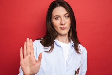 Serious young beautiful woman posing isolated over red wall background make stop gesture.