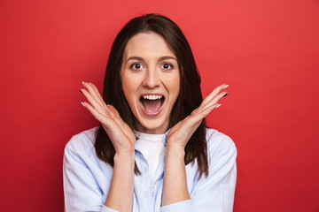Surprised emotional young beautiful woman posing isolated over red wall background.