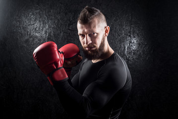 An athletic man wearing red kickboxing gloves posing and ready to fight in the gym