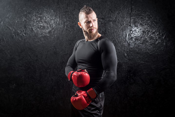An athletic man wearing red kickboxing gloves posing and ready to fight in the gym