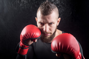 An athletic man wearing red kickboxing gloves posing and ready to fight in the gym