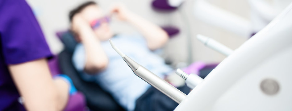 Blurred dental office. Tools are in the foreground. A boy with goggles in the dental chair