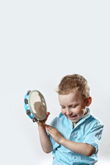 a cheerful boy in a blue shirt holding a tambourine and smiling on a light background