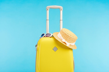 yellow colorful travel bag with straw hat and sunglasses isolated on blue - obrazy, fototapety, plakaty