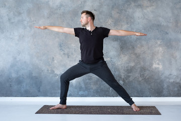 Man practicing yoga in studio doing Warrior 2 pose